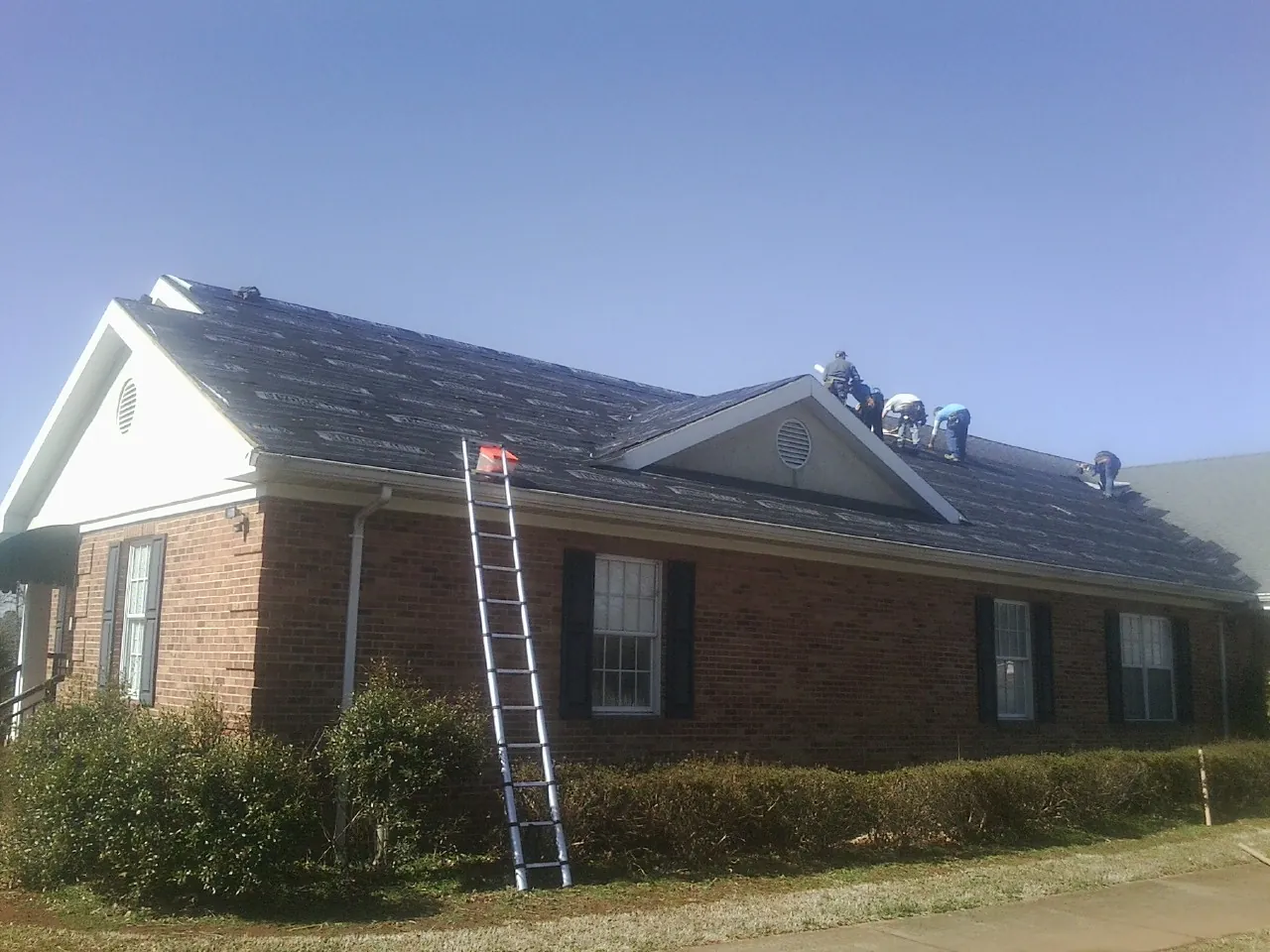 Crew tearing shingles off a brick ranch roof with a ladder set — Emergency Roof Repair work by our crew in North Chatham