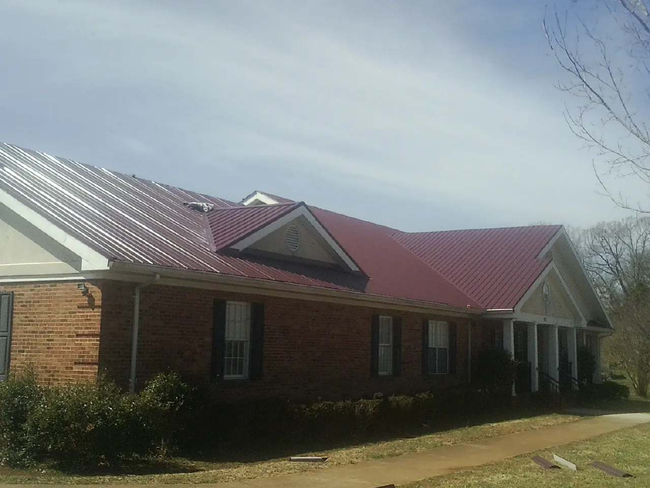 Red metal roof with gabled entries on a long brick building, from a Hail Damage Roof Repair job in North Chatham