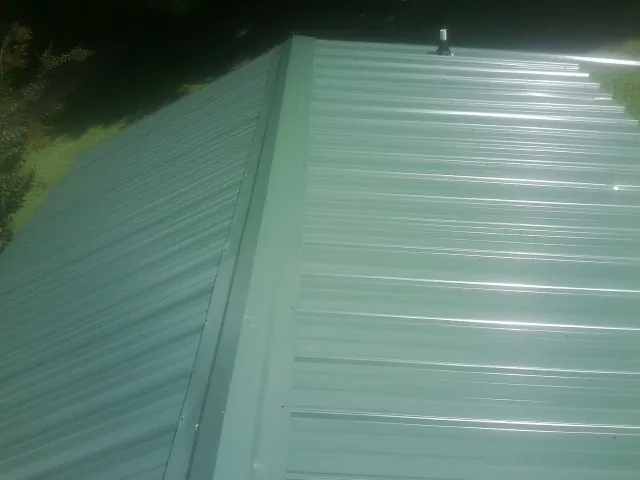 New green metal panels meeting at the ridge of a roof — Flat Roof Repair work by our crew in North Chatham