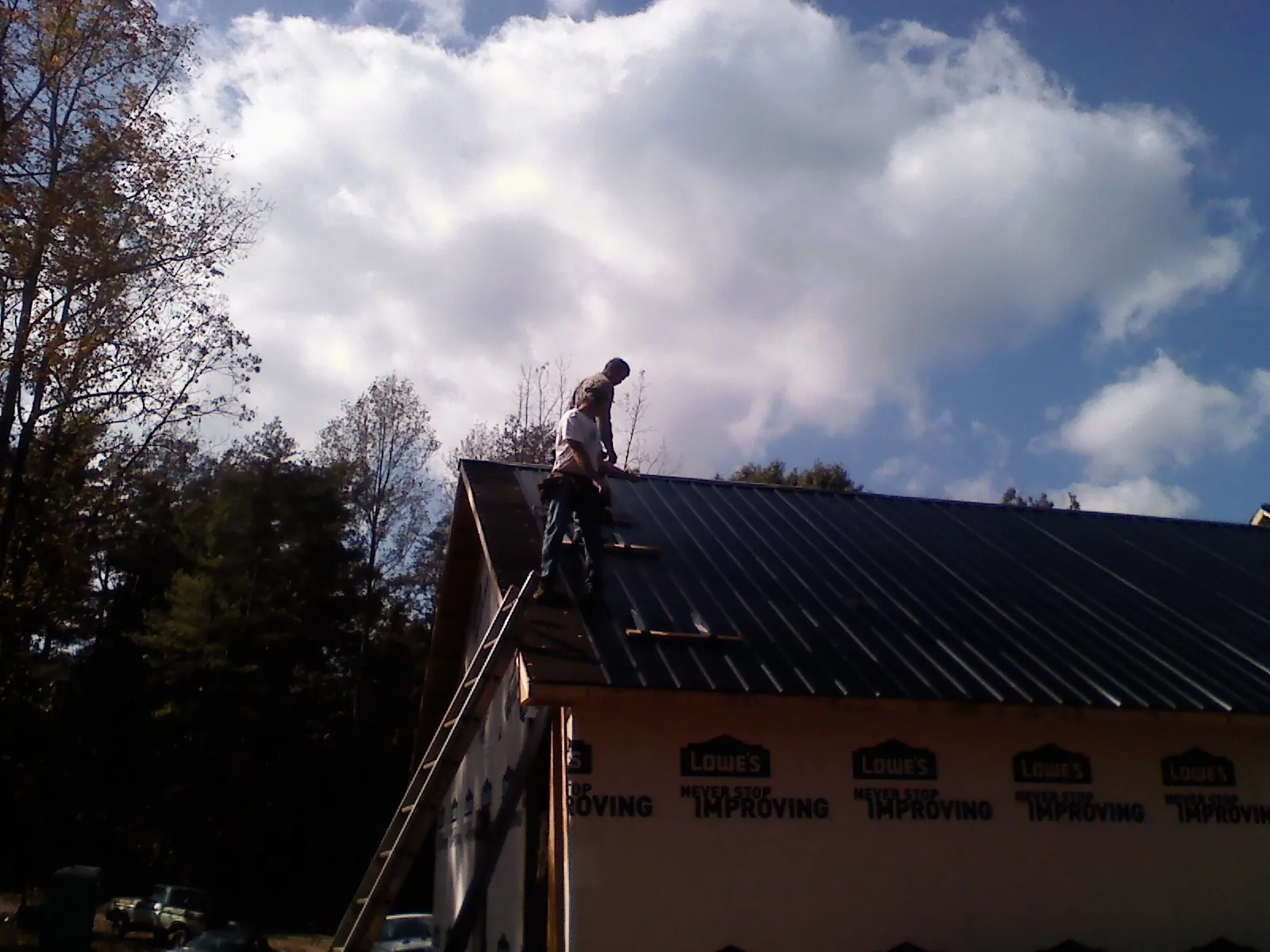 Roofer fastening dark metal panels high against a cloudy sky, from a Roof Inspection job in North Chatham