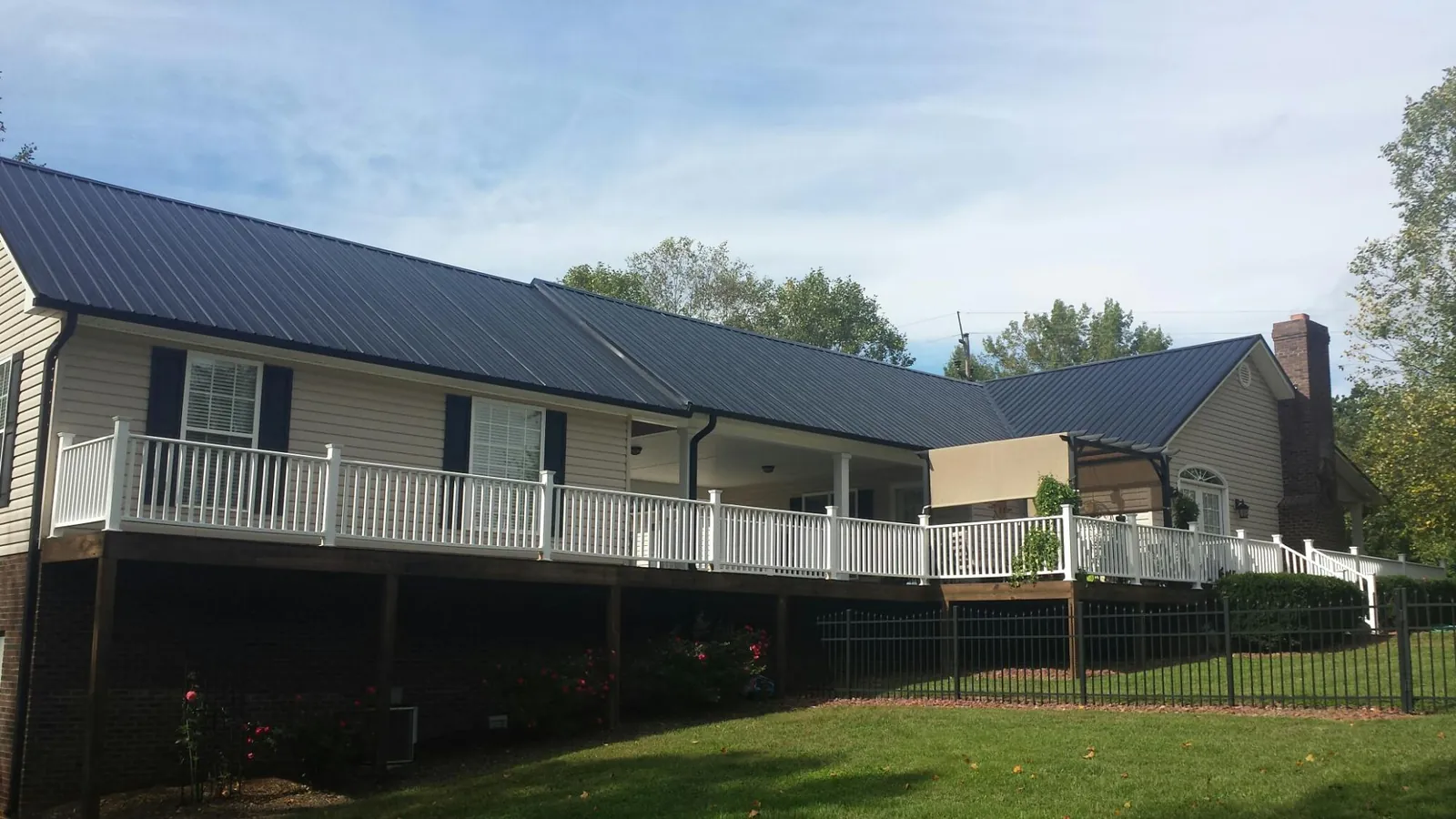 Black metal roof above a long white railed deck on a hillside home in North Chatham