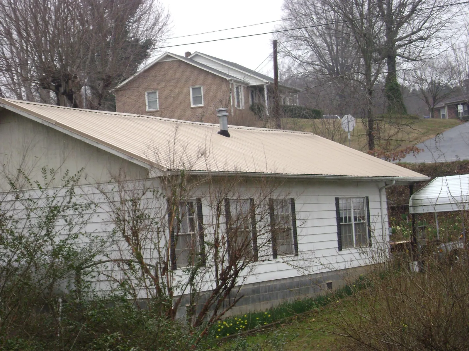 Tan metal roof on a white sided house set into a hillside — Commercial Roofing by Roofing Brothers in North Chatham