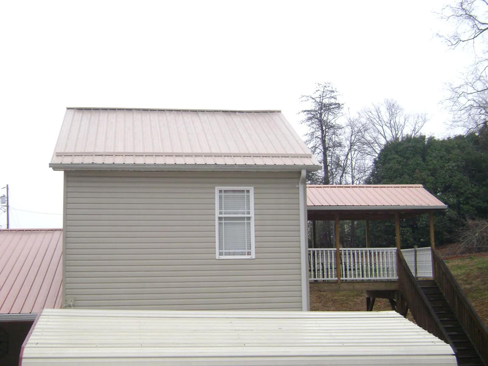 Tan metal roofs on a two story addition and attached porch, from a Roof Replacement job in North Chatham